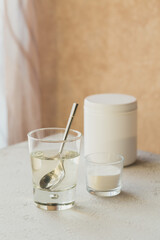 Glass with collagen dissolved in water and collagen protein powder on a light beige table. Healthy lifestyle concept.