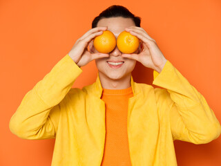 Asian man with oranges before eyes yellow jacket isolated background