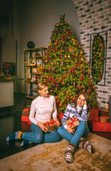 Two pretty women close up under the festive fir-tree indoors with the boxes of gifts.Christmas photo