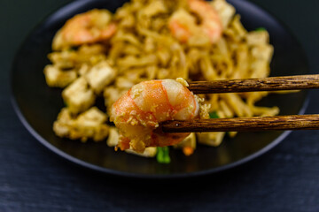 Black plate with pad thai on a slate board. Chopsticks with shrimp