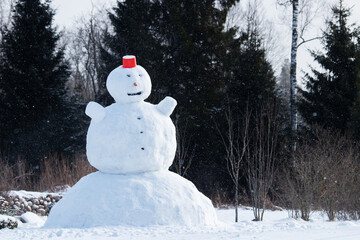 A giant snowman with a red bucket as a hat in Northern European garden during winter time. 
