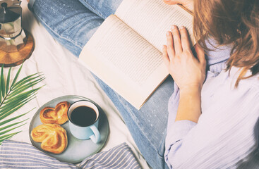 Woman having breakfast in bed and reading a book