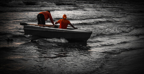 beach lifeguards with a rowing boat in stormy surf at evening