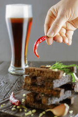man's hand holds pod of hot red pepper over rye croutons or beer snacks