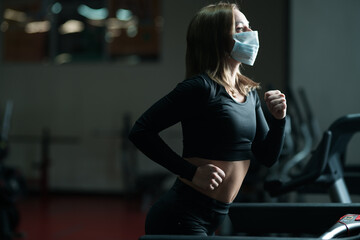 female athlete jogging on running track while wearing protective face mask in a gym during coronavirus epidemic. warm-up on a treadmill