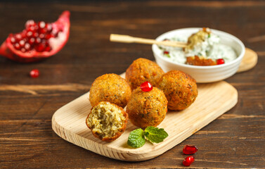 falafel, chickpea balls on a wooden Board with sauce and pomegranate seeds. Close-up on a dark wooden table