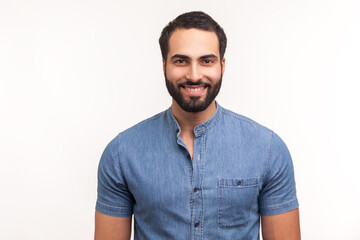 Fototapeta premium Positive handsome bearded man in blue shirt looking at camera with toothy smile, happy successful business man. Indoor studio shot isolated on white background