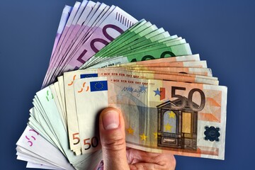 A rich man hand shows 20,000 Euros in 100 euro and 500 euro banknotes on a blue background