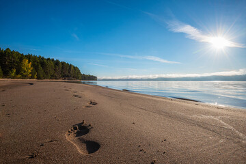 Bare footprints on the sand by the river, Sunny morning and fog over the water, sun rays.