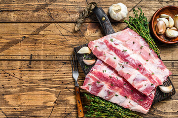 Fresh raw pork rack spareribs with thyme and garlic on cutting board. wooden background. Top view. Copy space