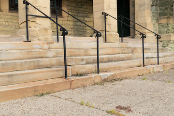 Decaying limestone stairs and columns of an old church entry, black railings and patchwork, horizontal aspect