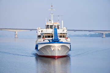 small passenger ship on the river and road bridge in the morning haze in the background © Evgeny