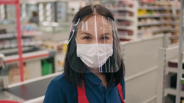 Close-up portrait of attractive mixed-race woman in plastic face shield working as cashier in supermarket during pandemics