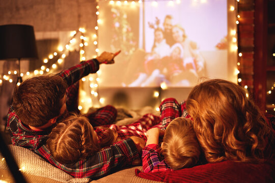 family mother father and children watching projector, film, movies with popcorn in   christmas evening   at home.