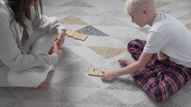 Mom and son play at home in wooden dominoes during carantite covid-19.