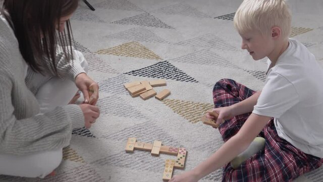 A woman and a boy play dominoes at home on the floor. Family leisure mom and son during lockdown