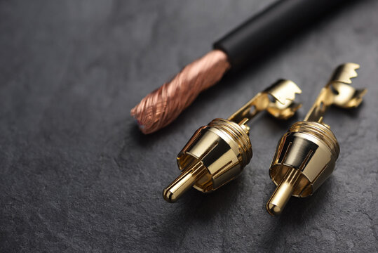 Golden RCA connector and cable on black slate background.