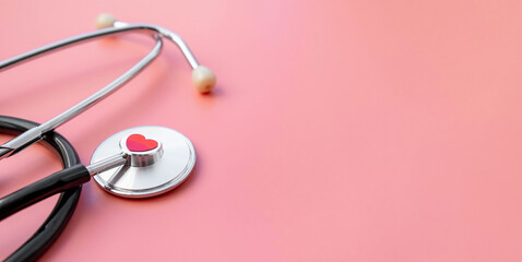 Fototapeta premium Black stethoscope with red heart of doctor for checkup on pink background. Stethoscope equipment of medical use. Health care and cardiology concept with copy space. Valentines day