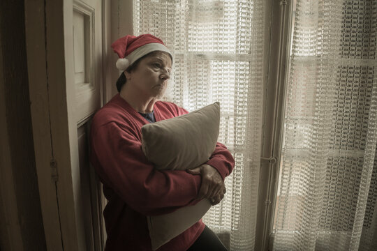 Senior Woman Having Sad Christmas Alone - Mature Retired Lady 60s Or 70s In Santa Claus Hat Depressed And Emotional At Home Feeling Lonely And Melancholic