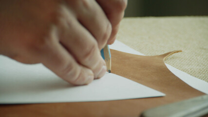 Close-up pencil outlines the pattern and marks a piece of genuine leather for cutting to create an exclusive product.