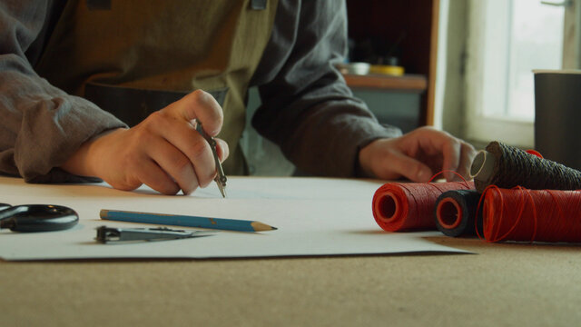 Close-up tailor makes markings on a sheet of paper with a pencil and compasses for making patterns for sewing products made of genuine leather. - Powered by Adobe