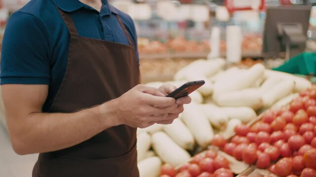 Midsection footage of unrecognizable male worker of grocery section in hypermarket using smartphone on work