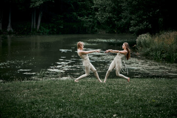 Two beautiful slender girls dancing in nature. On the background of the lake. The concept of natural cosmetics and harmony with nature. My hair is blowing in the wind.