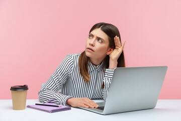 I can't hear you. Business woman holding arm near ear trying to listen secret talk on video call on laptop, bad internet connection, online conference. Indoor studio shot isolated on pink background