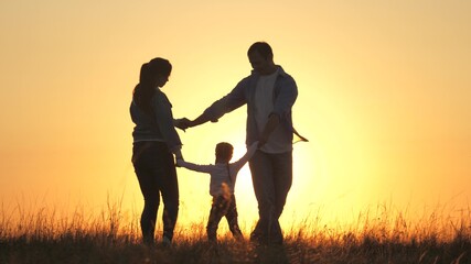 Fototapeta na wymiar young mom, dad with a healthy daughter dance in a circle under warm sun, have fun in field. happy family, holding hands, plays in the park on grass, at sunset. Family and childhood concept.