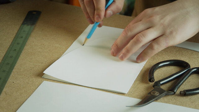 Close-up of creating patterns for the production of handmade clothing. A hand with a pencil draws a curved line.