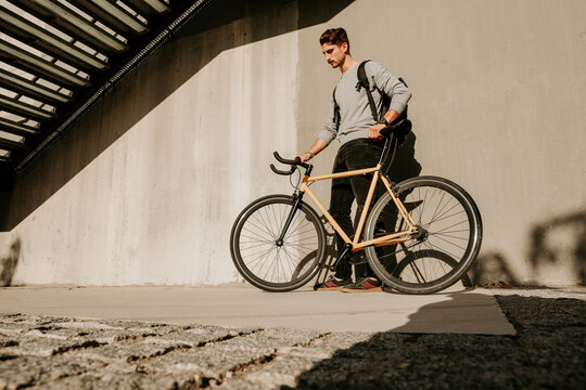 Caucasian young guy in casual clothes posing with bike over wall. Outdoor.