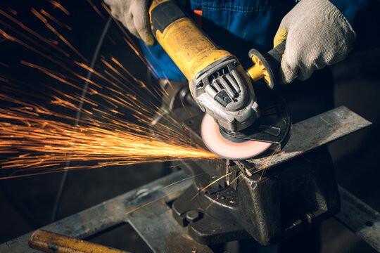 Locksmith in special clothes and goggles works in production. Metal processing with angle grinder. Sparks in metalworking