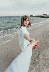 Fototapeta na wymiar beautiful girl holds the guy's hand. follow me to the sea. young people in love. happy girl. sea on background. rest by the sea