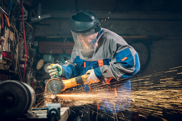 Locksmith in special clothes and goggles works in production. Metal processing with angle grinder....
