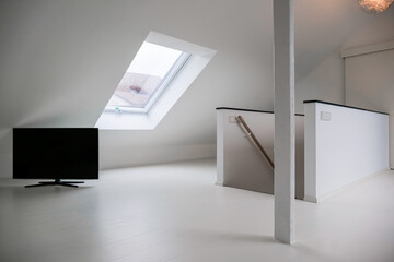 Moderner LED Fernseher stehend am Boden im weissem Raum mit Dachfenstern und Treppen 