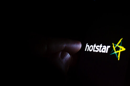 Hotstar Streaming Service Logo On The Screen In A Dark Room And A Hand Pointing At It. Hotstar Is An Indian Streaming Service.