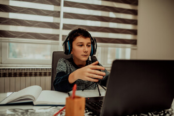 Boy attending online classes from home. Child using laptop and headsets for connecting with teacher and schoolmates. School education and social distance during quarantine