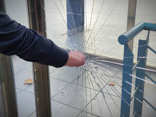 A violent, vandal,angry person breaks and destroys a window with a punch