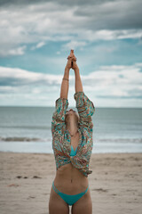 Young blonde woman in yoga stretching on beach. Blue bikini. Sun salutation.