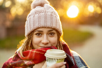 Young woman with coffee cup smiling outdoors during winter
