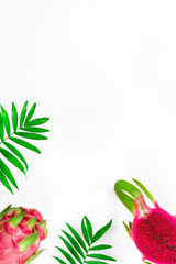 Creative flat layout with fresh organic pink dragon fruit, pitaya or pitahaya, on white background with copy-space. Trendy top view, flat lay of this exotic fruit cut in half with palm leaves.