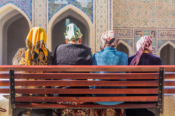 BUKHARA, UZBEKISTAN - MAY 1, 2018: Local women sit on a bench at the Kalyan Mosque in Bukhara, Uzbekistan - obrazy, fototapety, plakaty