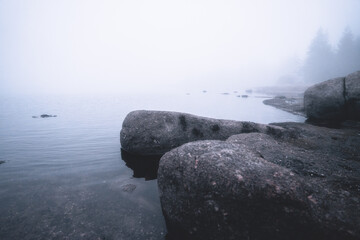 Coastal landscape of foggy lake. Stones in the water on foreground. Long exposure shot.