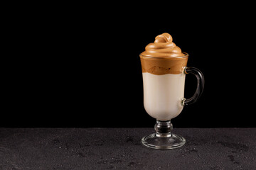 Cup Dalgona coffee on dark wet tabletop, close-up. Table with water drops. Popular Korean drink with a high figured foam of instant coffee. Black background, place for text
