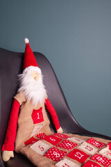 Excited Santa Claus toy sitting on a chair on a dark green background in Christmas hat red coat Happy New Year celebration merry holiday concept