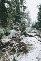 Romantic couple sitting on rock and watching the snow in forest