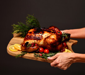 Woman hands hold plate with cooked thanksgiving turkey or chicken for christmas dinner evening with on wooden rustic plate garnished with cherry berries and fruits on dark background