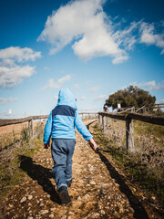 Niño o chico con abrigo caminando bajo un cielo azul con nubes