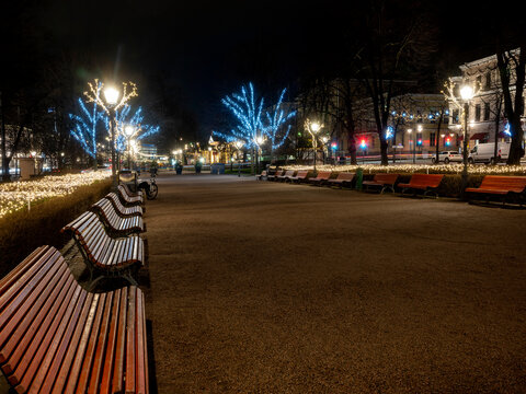 A beautiful view of a public park with Christmas lights and decorations. A row of wooden beches.