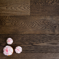 Three cupcakes in a corner of a wooden table; small and large cupcakes topped with pink soft icing, sprinkles and pearls